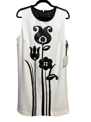 A fashion model showcases the front view of the Victoria Beckham for Target black and white tulip shift dress. The sleeveless dress features a crisp cream-white base color accented by a bold, graphic faux-leather black tulip floral appliqué placed vertically down the center body, highlighting the vintage-inspired design.