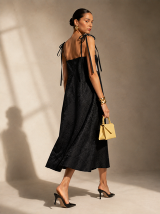Back profile view of black Sister Jane Fanciful Flower midi dress showcasing adjustable double-tying satin ribbon shoulder straps.
